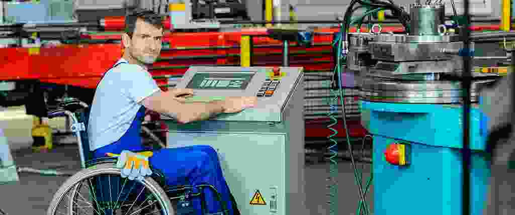 Man in wheel chair working with industrial equipment in factory setting