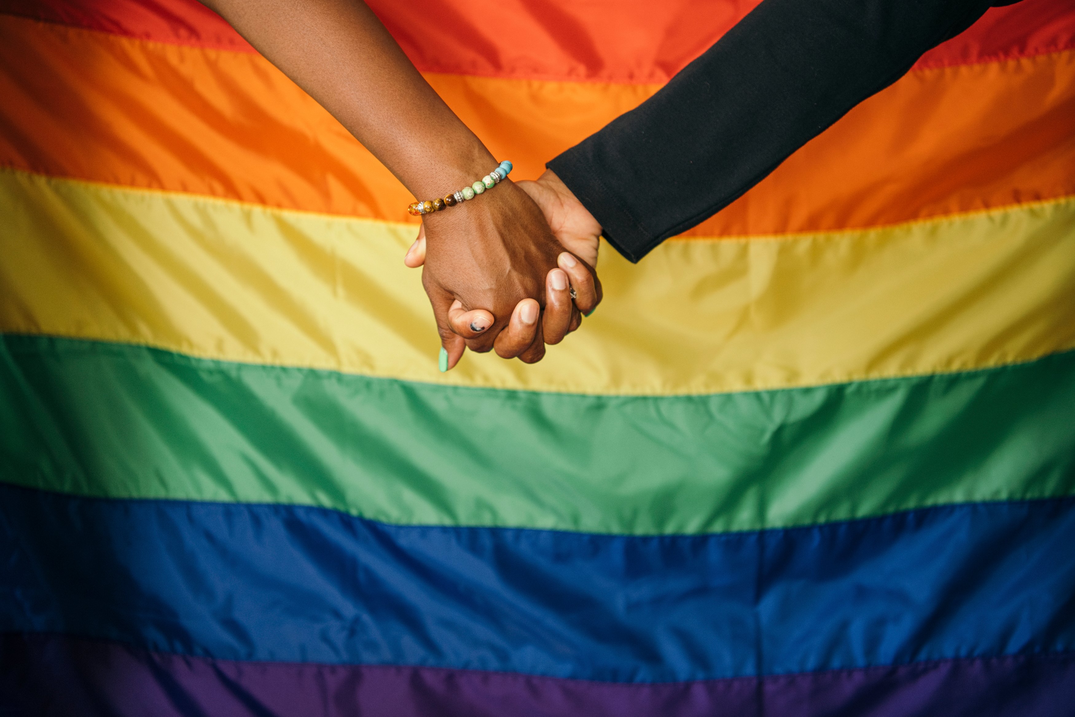 black hand and white hand holding hands in front of pride flag
