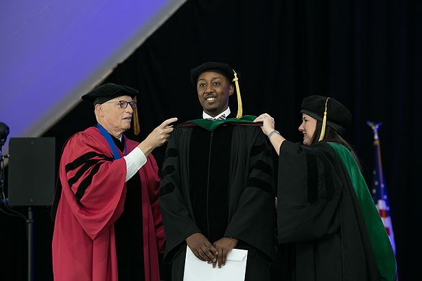 SOM graduate Robert Gakwaya is hooded by Michael Hirsh and Cynthia Ennis.