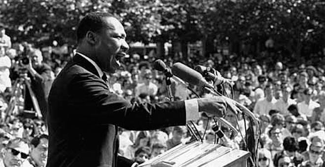 image of Martin Luther King Jr. speaking at a podium outdoors in front of a large crowd