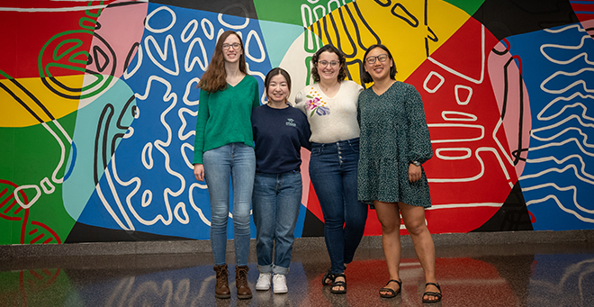 Four students in front of a colorful mural