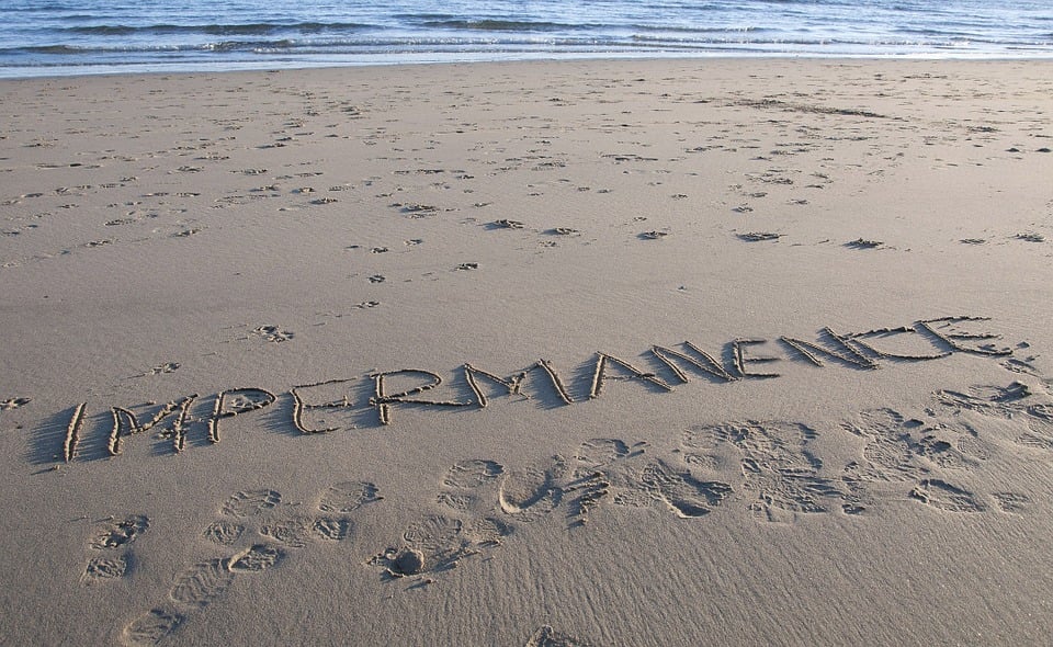 The word impermanence written on a sandy beach
